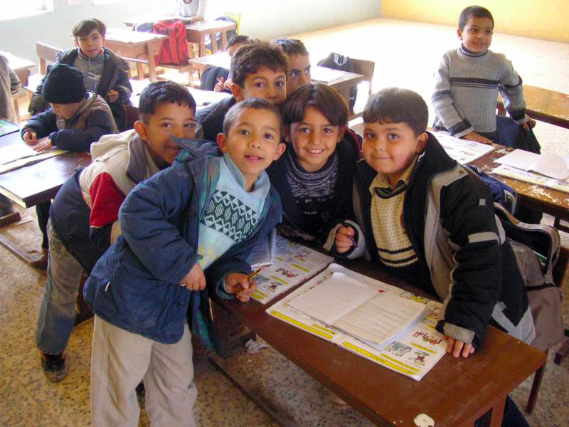 A photo of boys crowding around a school desk for picture. At Theodor Schneller School, Marka, Jordan